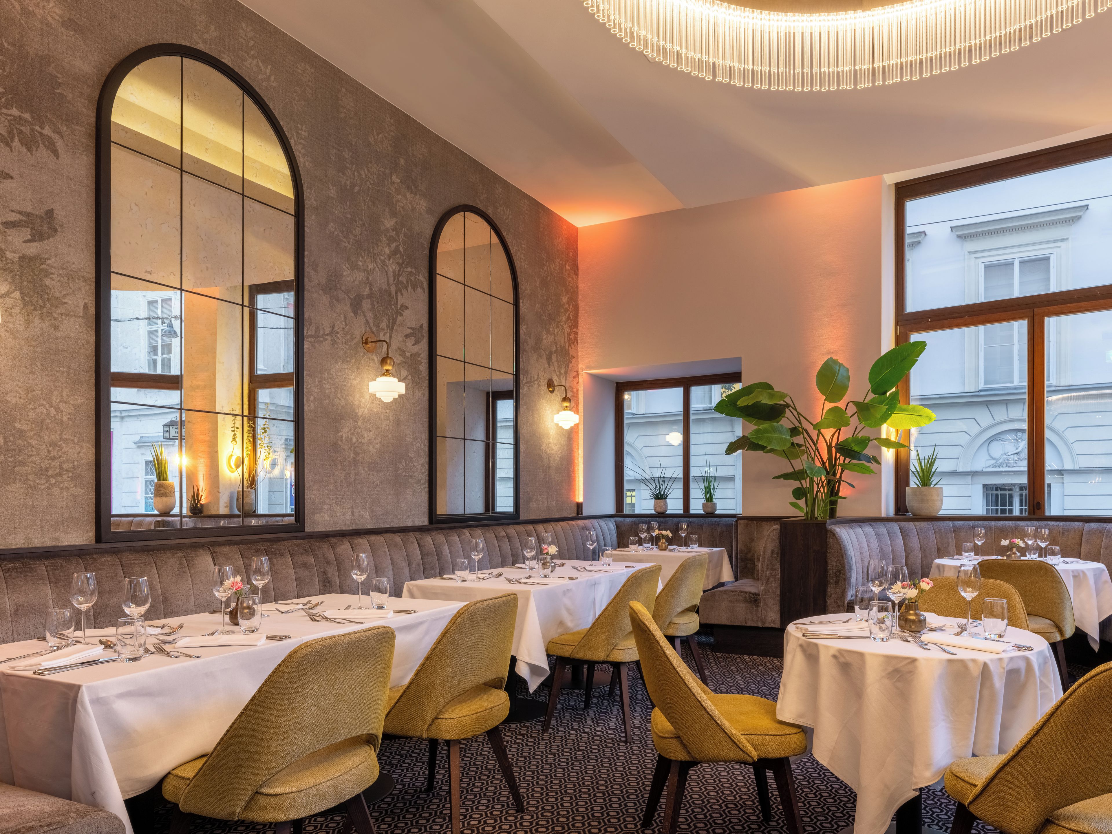 Interior de restaurante com mesas postas para refeições, grandes janelas em arco e um lustre.