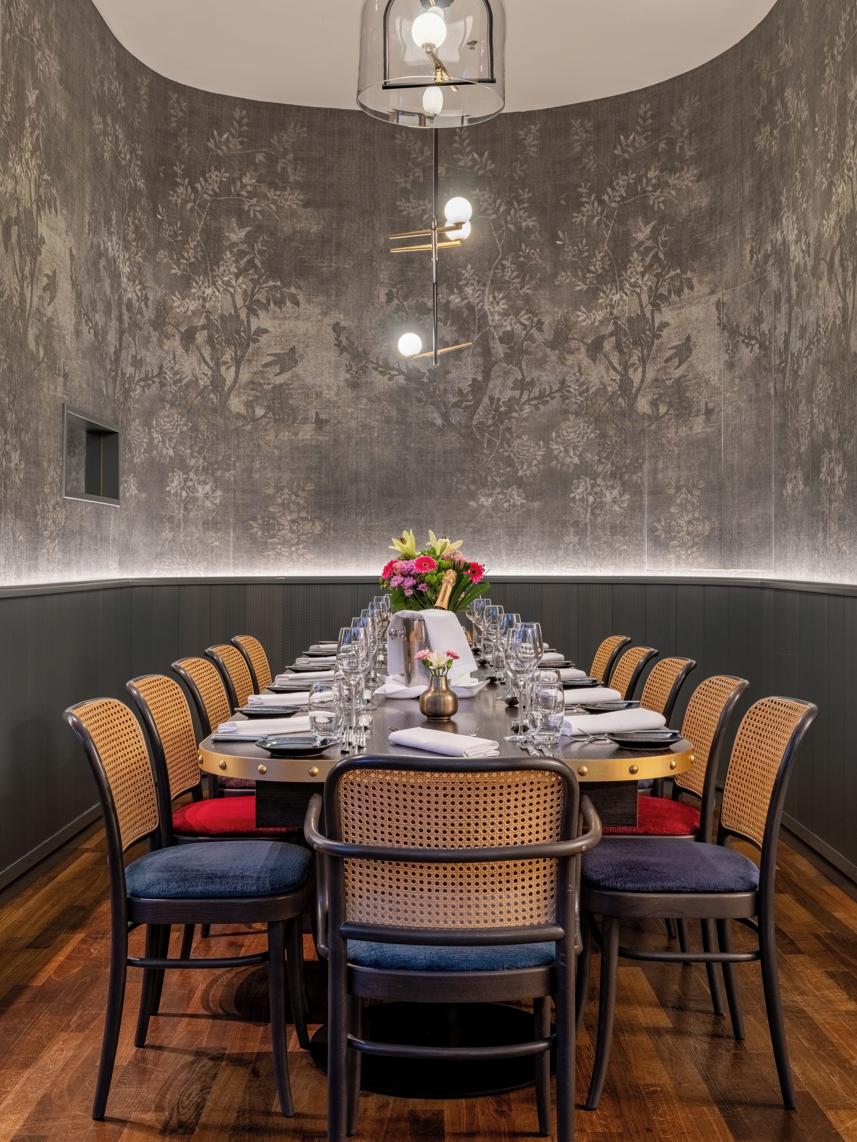 Un coin repas avec une longue table dressée pour le repas, entourée de chaises en osier dotées d’assises rembourrées.