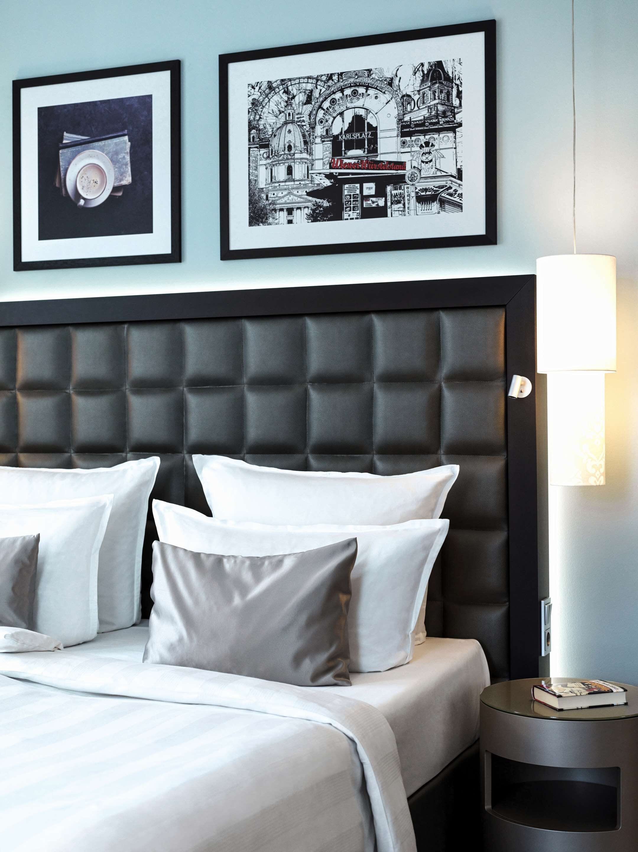 A hotel room with a tufted headboard, white bedding, and a framed black and white cityscape picture.