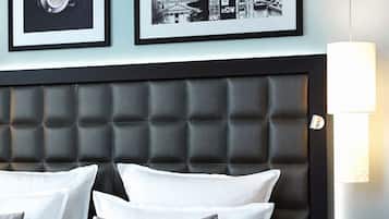 Ett hotellrum med en stoppad sänggavel, vita sängkläder och en inramad svartvit bild av en stadsbild.