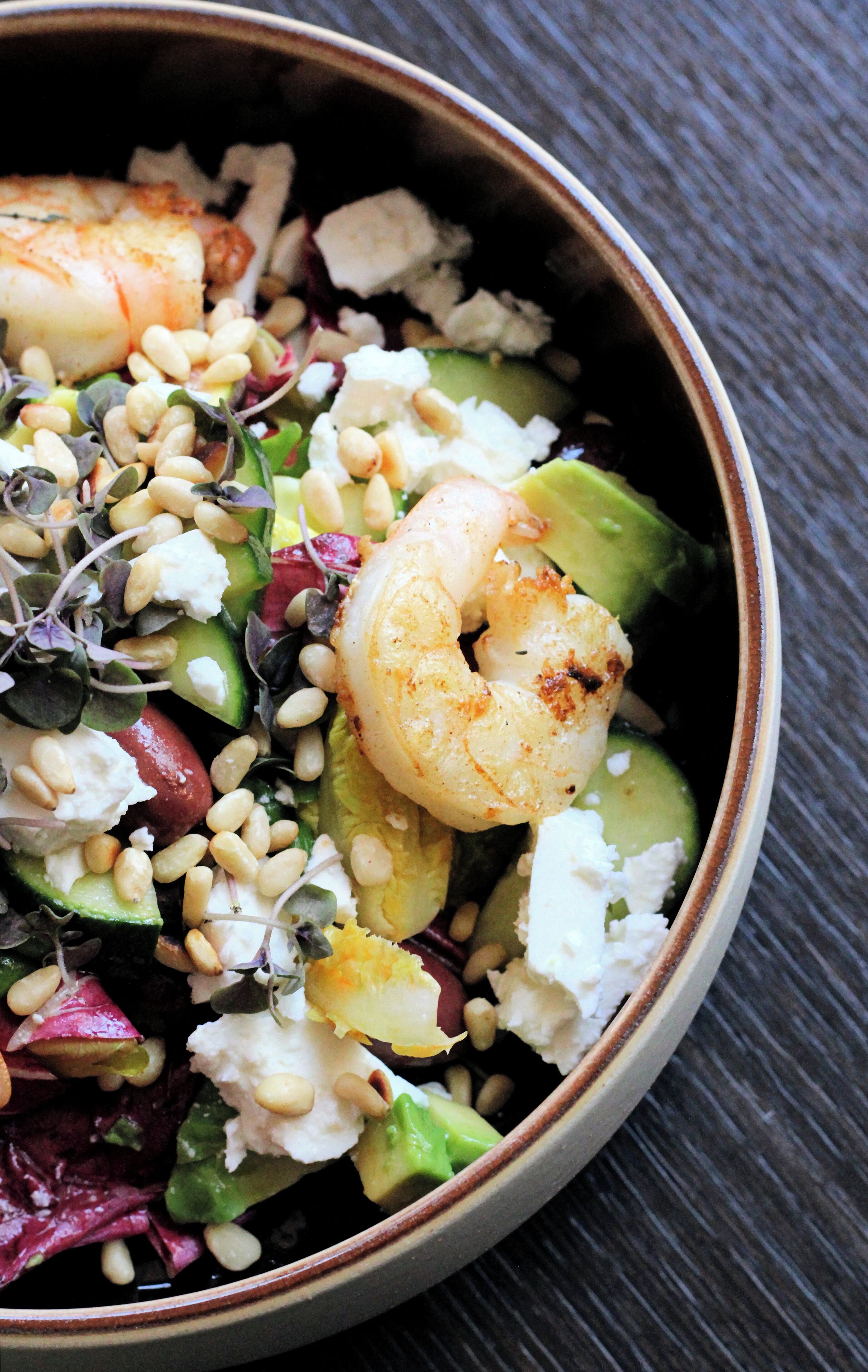 Een saladekom met garnalen, avocado, noten en kaas.