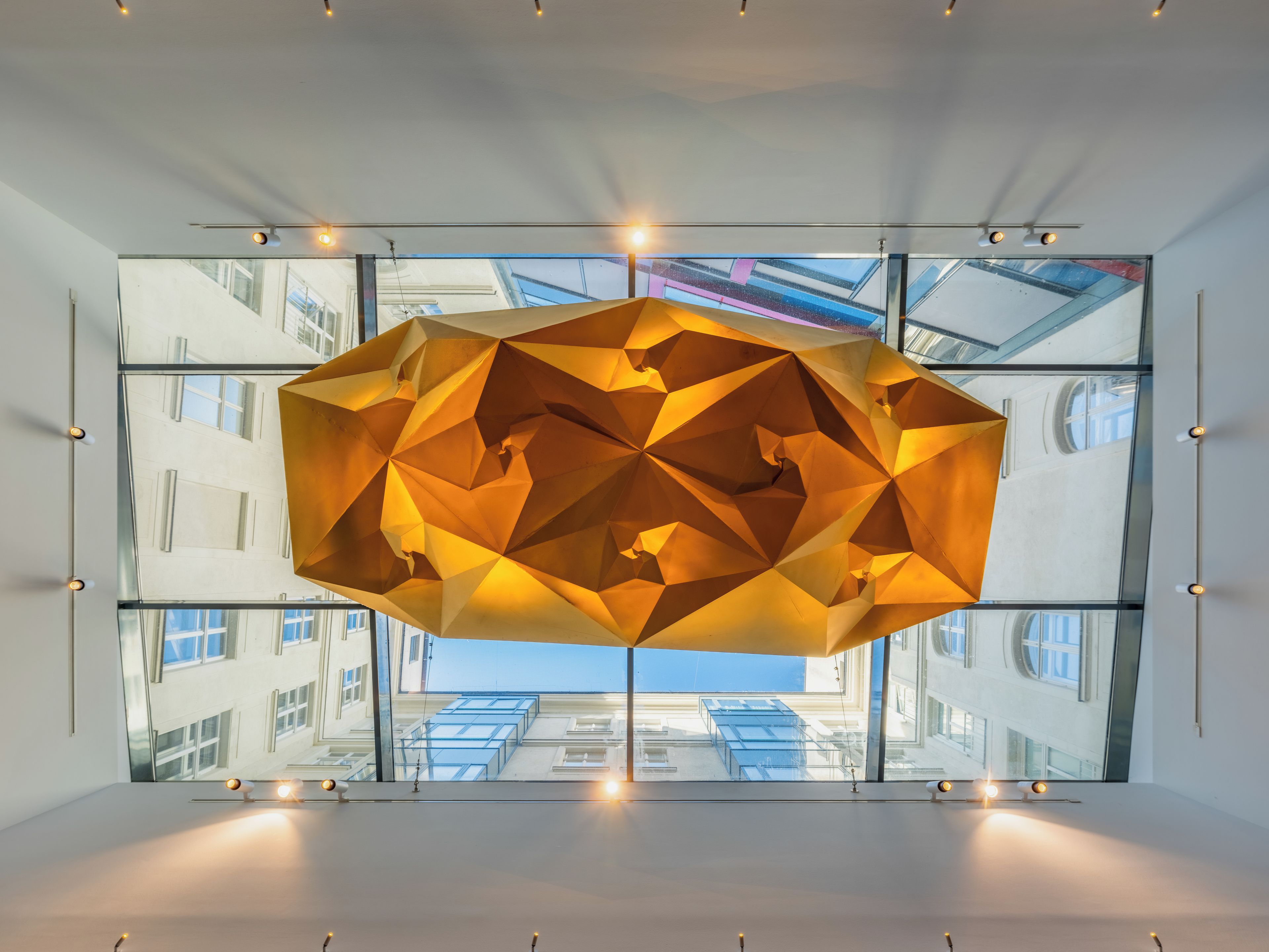 Een modern interieur met een geometrische lamp en grote ramen met uitzicht op het exterieur van een gebouw.