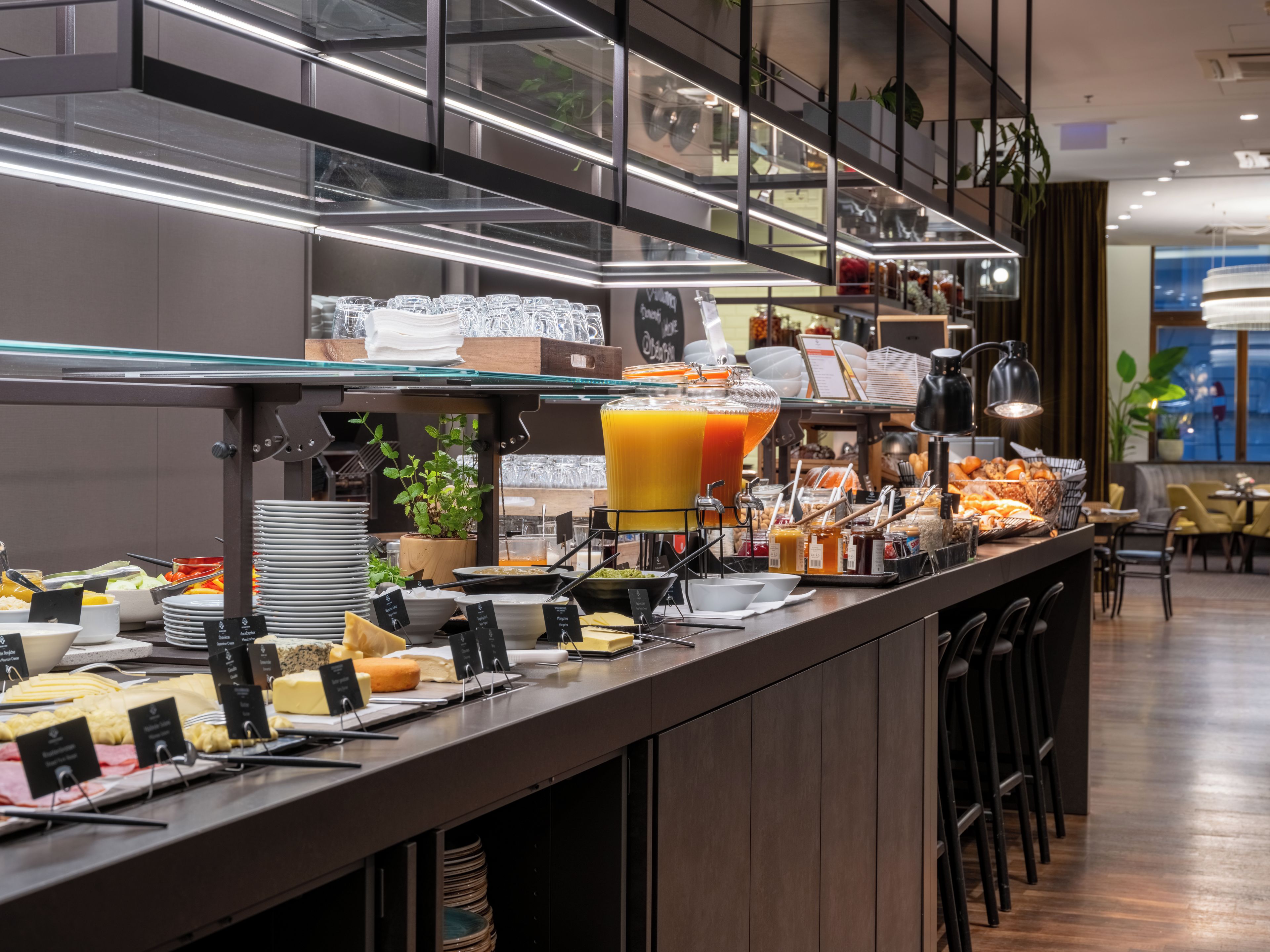 Bar de buffet com diversos alimentos e um grande dispensador de sucos.
