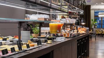 Bar de buffet com diversos alimentos e um grande dispensador de sucos.