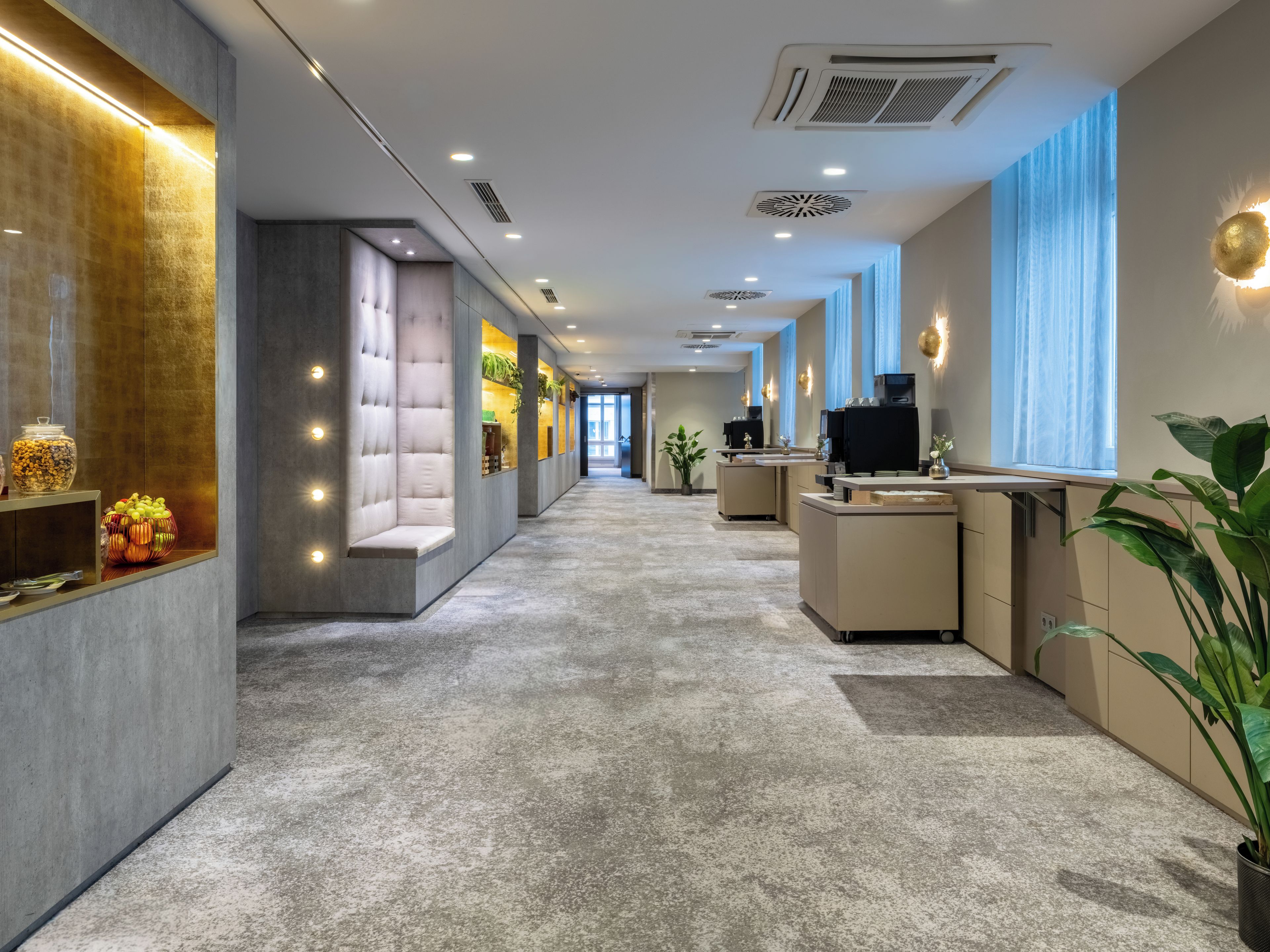 A modern hotel lobby with a long corridor, seating areas, and a reception desk.