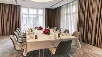 Ein Konferenzraum mit langem Tisch, gedeckt für eine Besprechung, umgeben von Stühlen, mit großen Fenstern und Vorhängen.