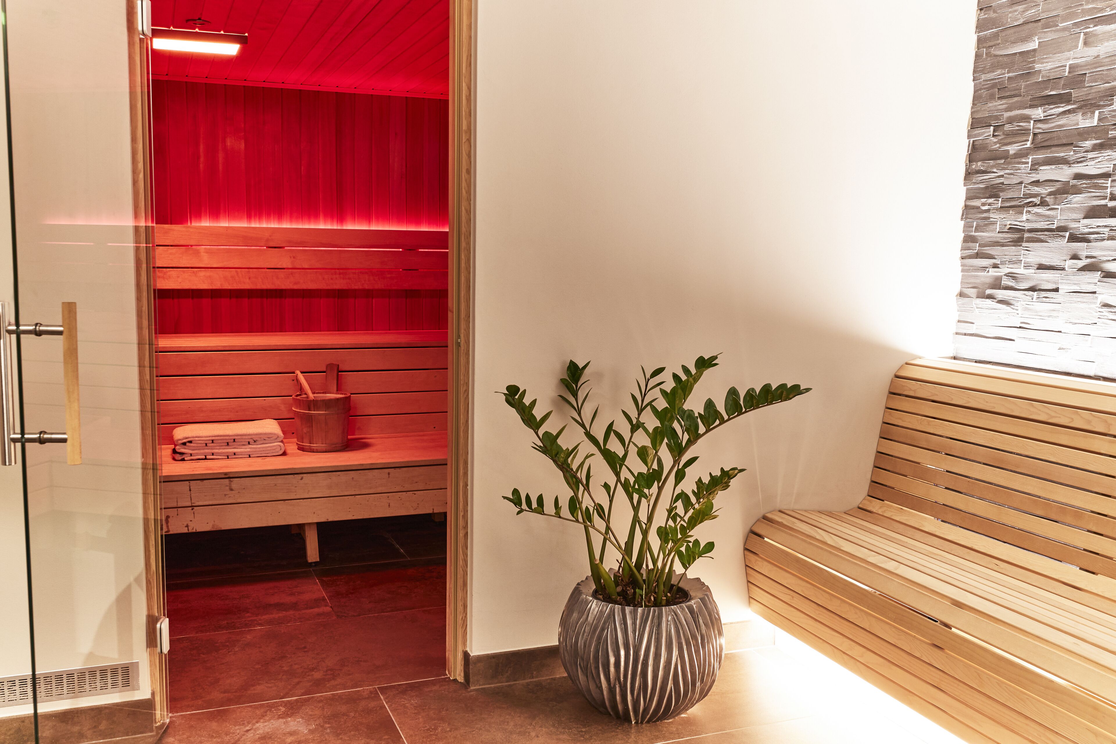 A spa area with a red-lit wall, a wooden bench, and a potted plant.