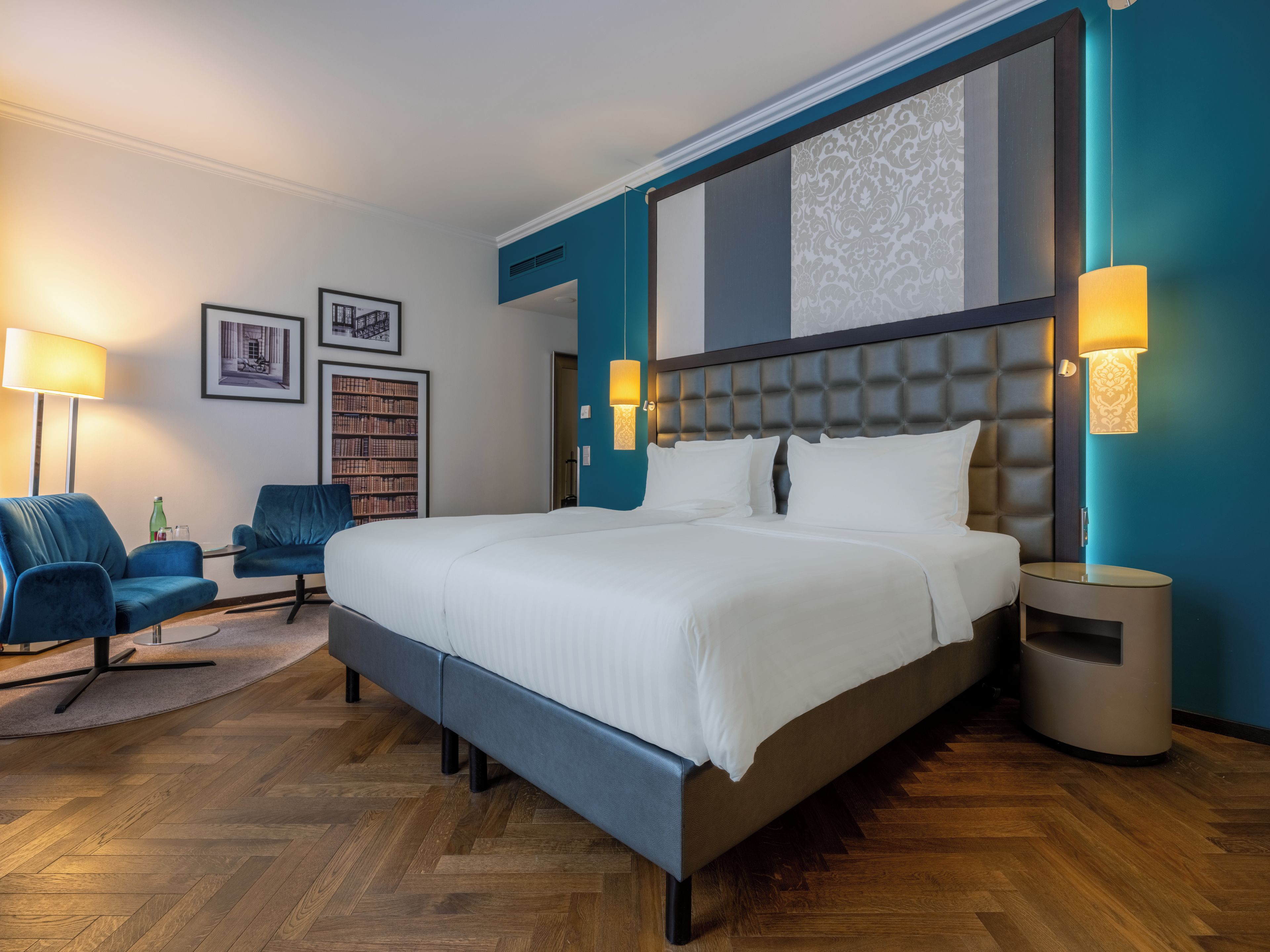 Ett modernt hotellrum med en stor säng, två fåtöljer, ett sidobord och en bokhylla.
