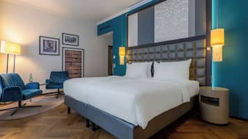 Ett modernt hotellrum med en stor säng, två fåtöljer, ett sidobord och en bokhylla.
