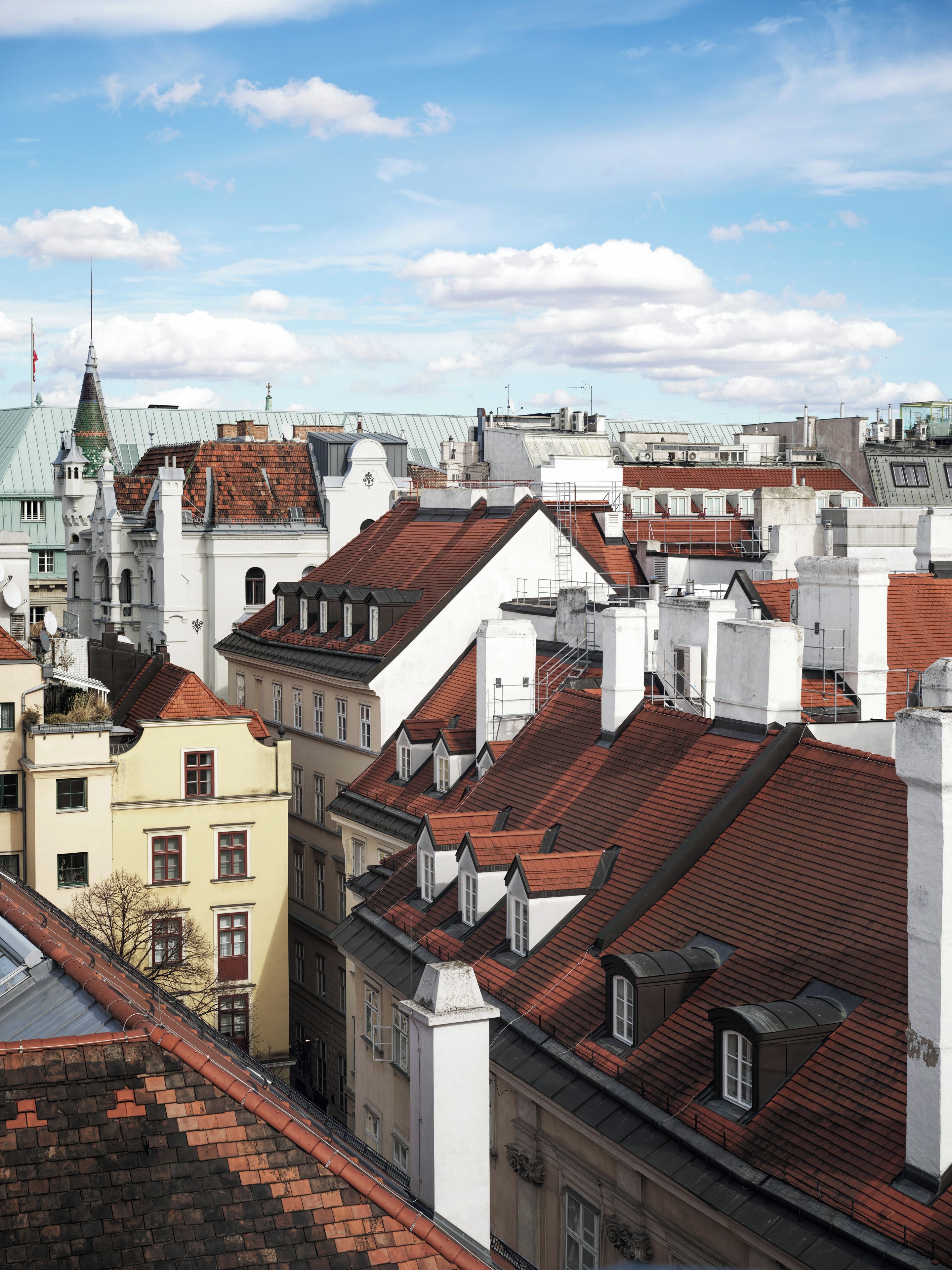 A cityscape with a variety of building rooftops, including some with dormer windows and chimneys.