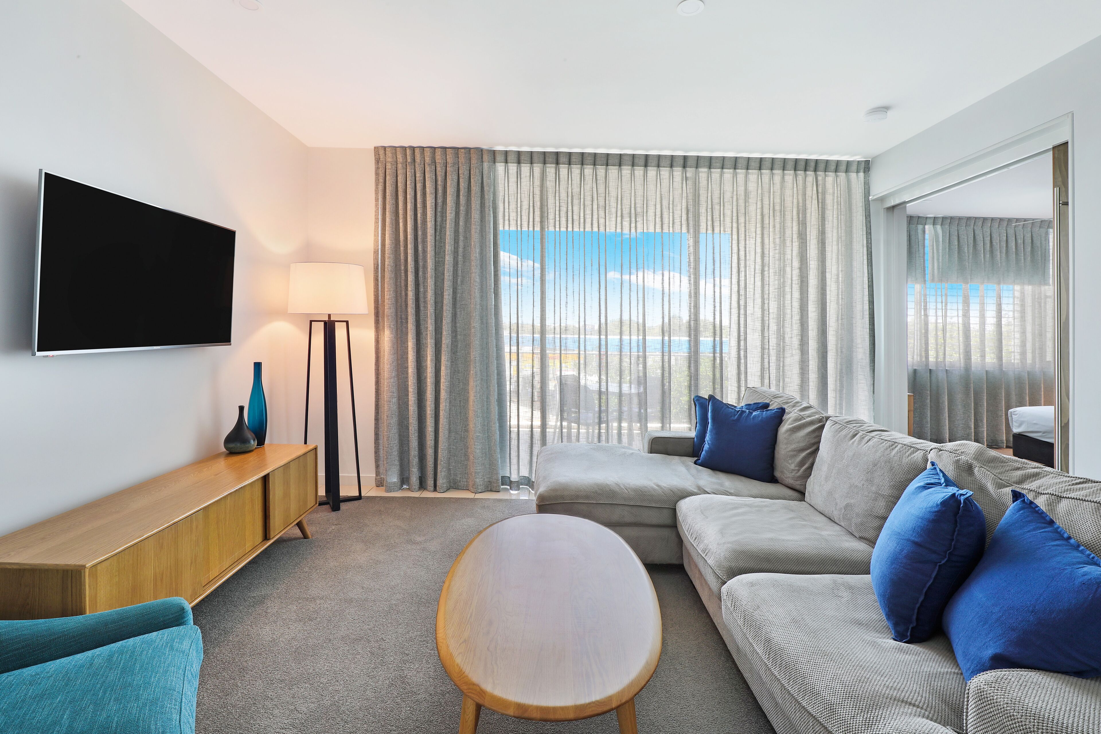 Ein modernes Hotelzimmer mit einer großen Couch, einem Holztisch und einem Flachbildfernseher.