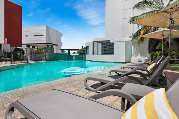 A swimming pool with lounge chairs and umbrellas, surrounded by modern buildings. - Element on Coolum Beach (Coolum Beach)