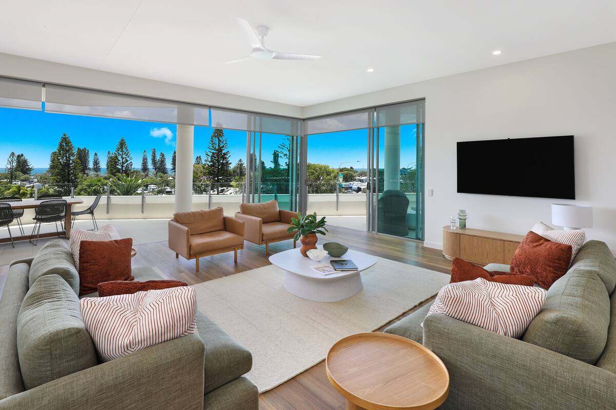 A modern living room with a large window, a flat-screen TV, and a ceiling fan.