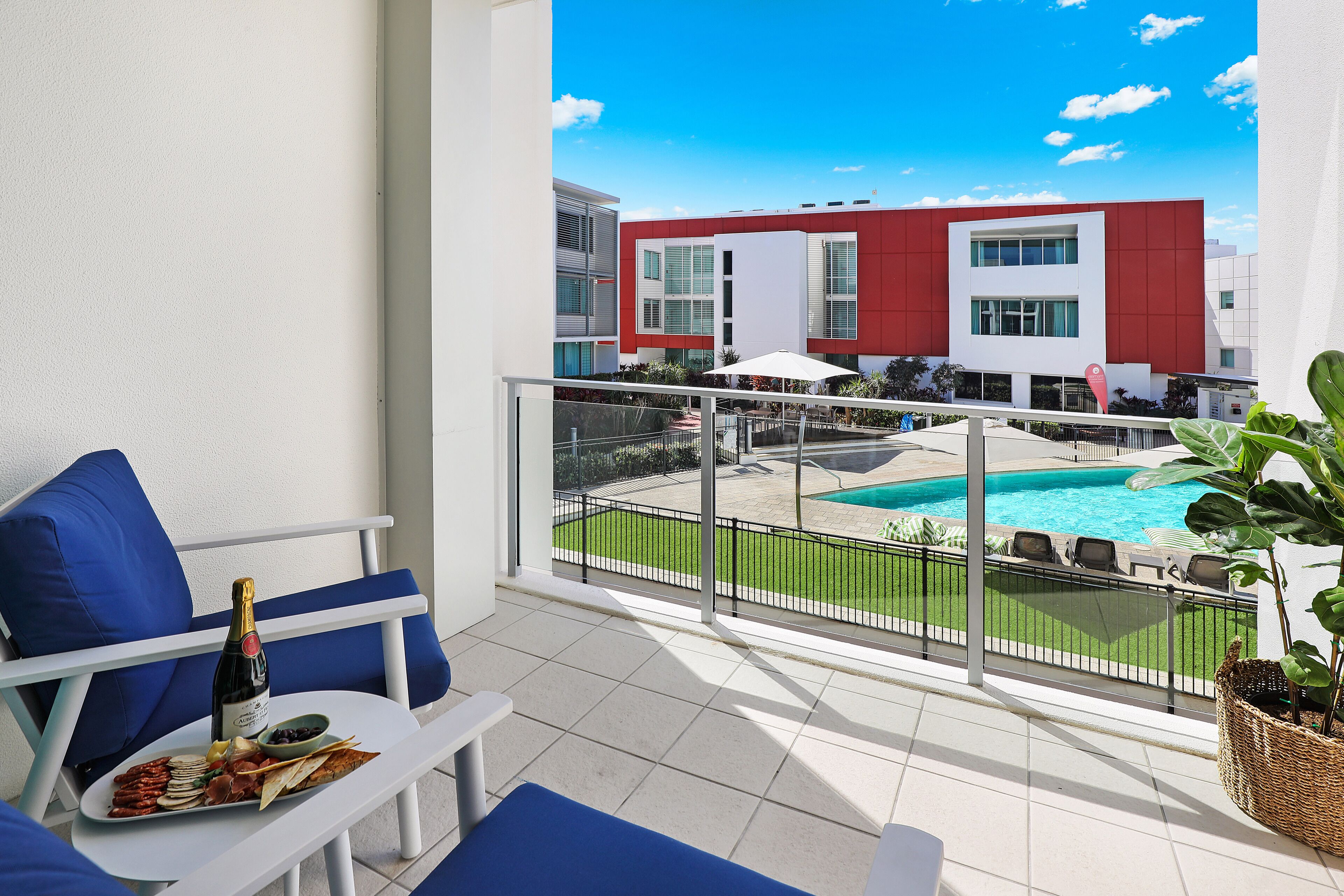 A balcony with a white table, blue chairs, and a bottle of champagne.