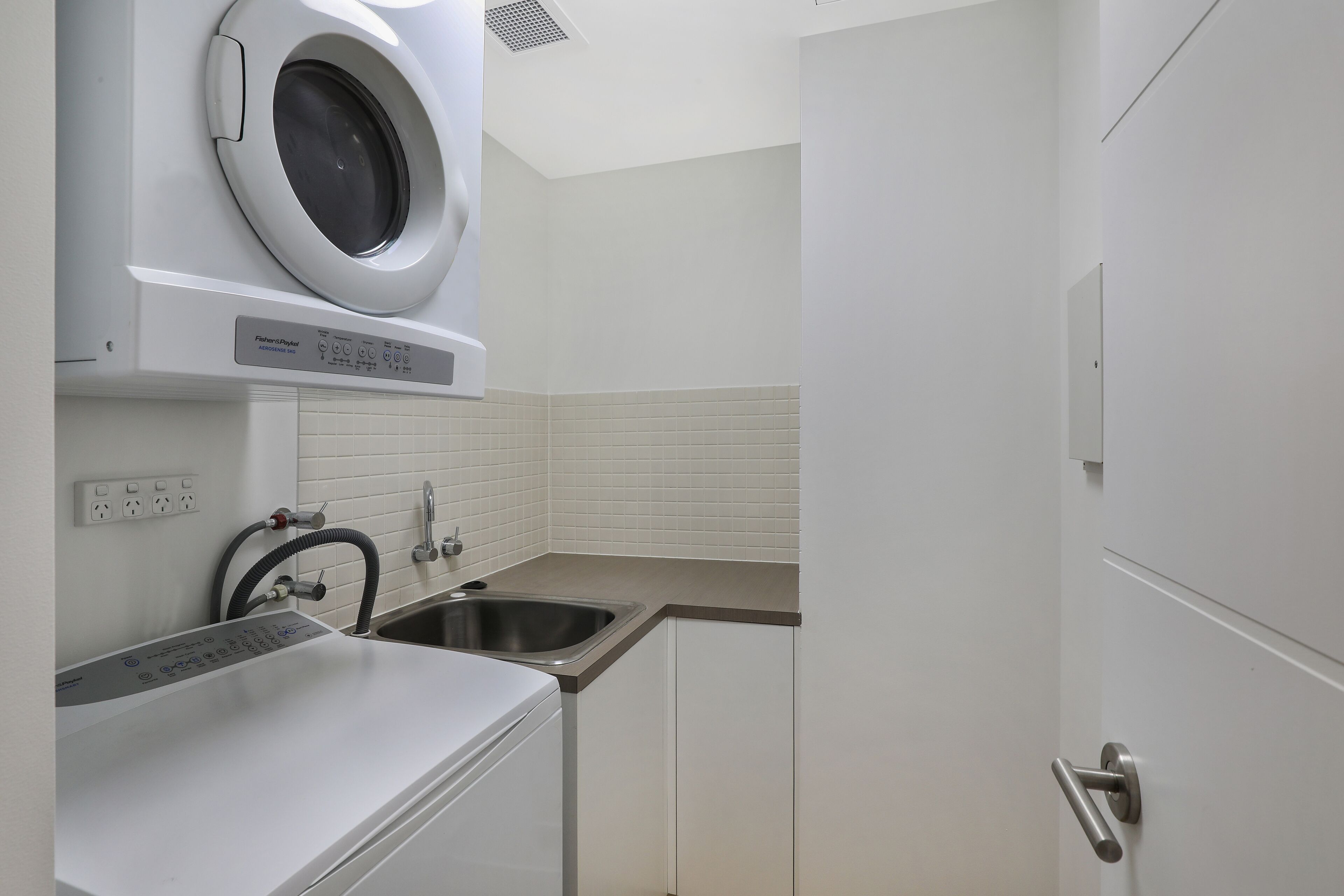 A compact kitchen with a built-in washer and dryer, a sink, and a door with a handle.