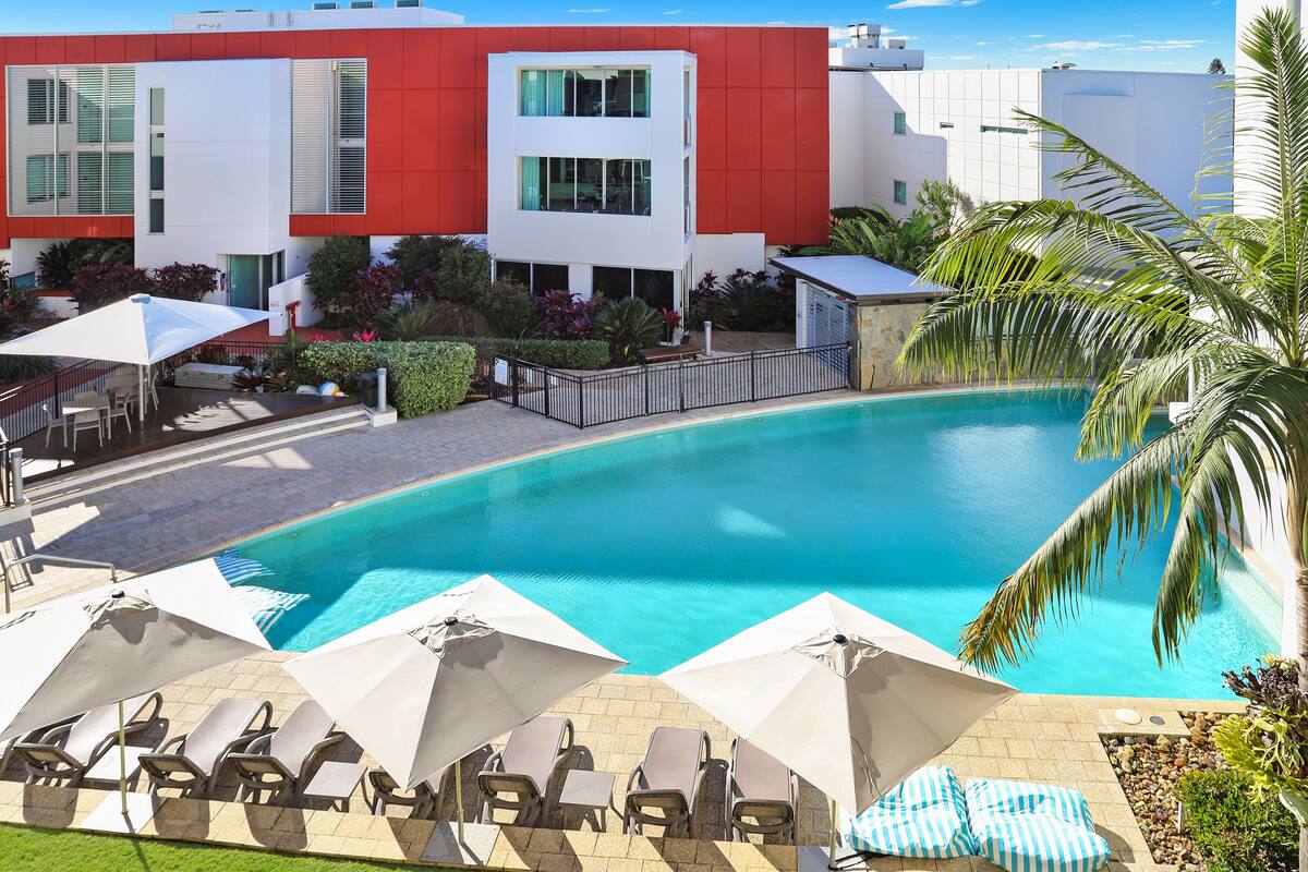 A modern hotel with a swimming pool, sun loungers, and umbrellas.