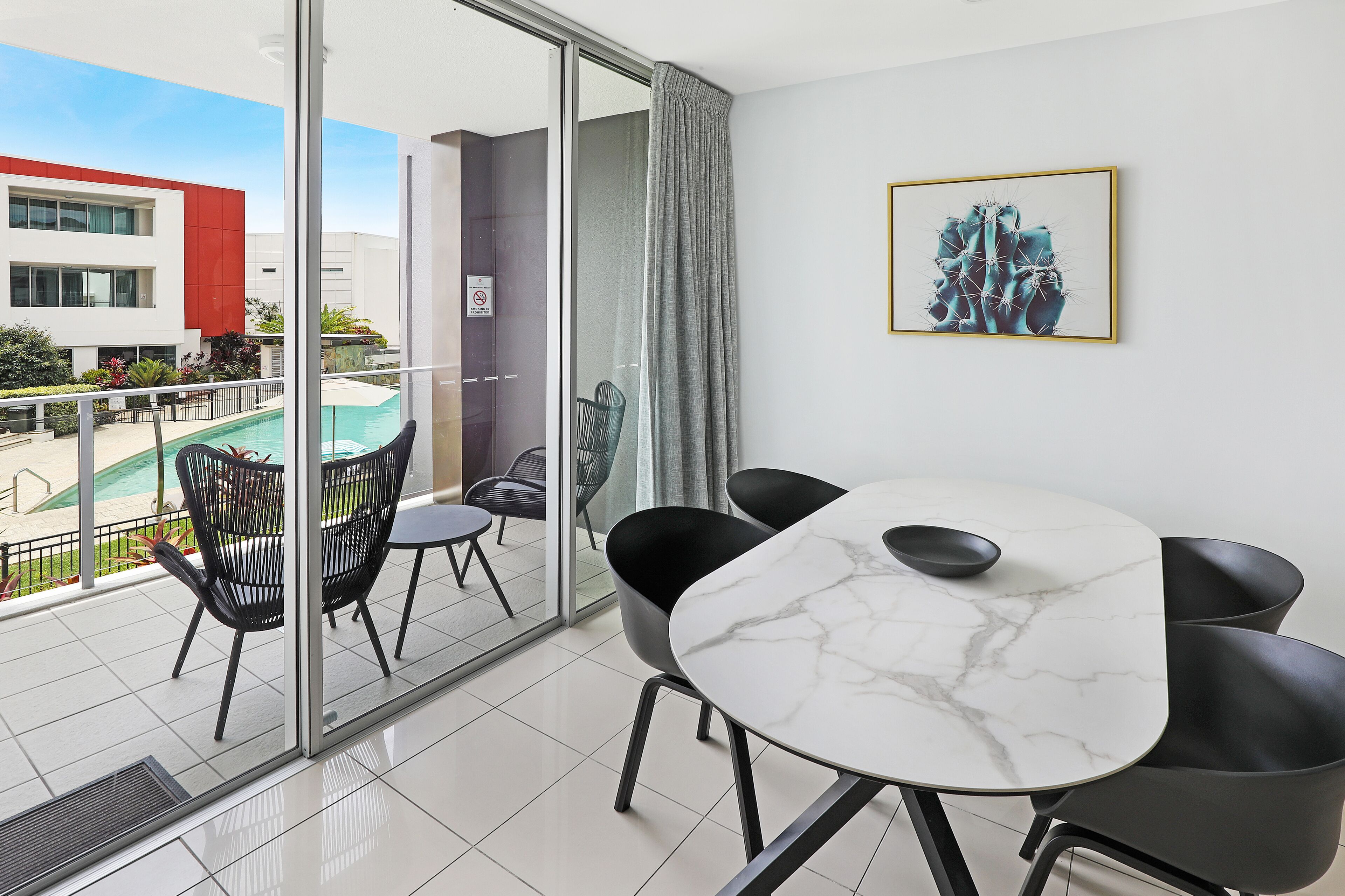 A modern room with a glass door leading to a balcony, a marble table, and black chairs.