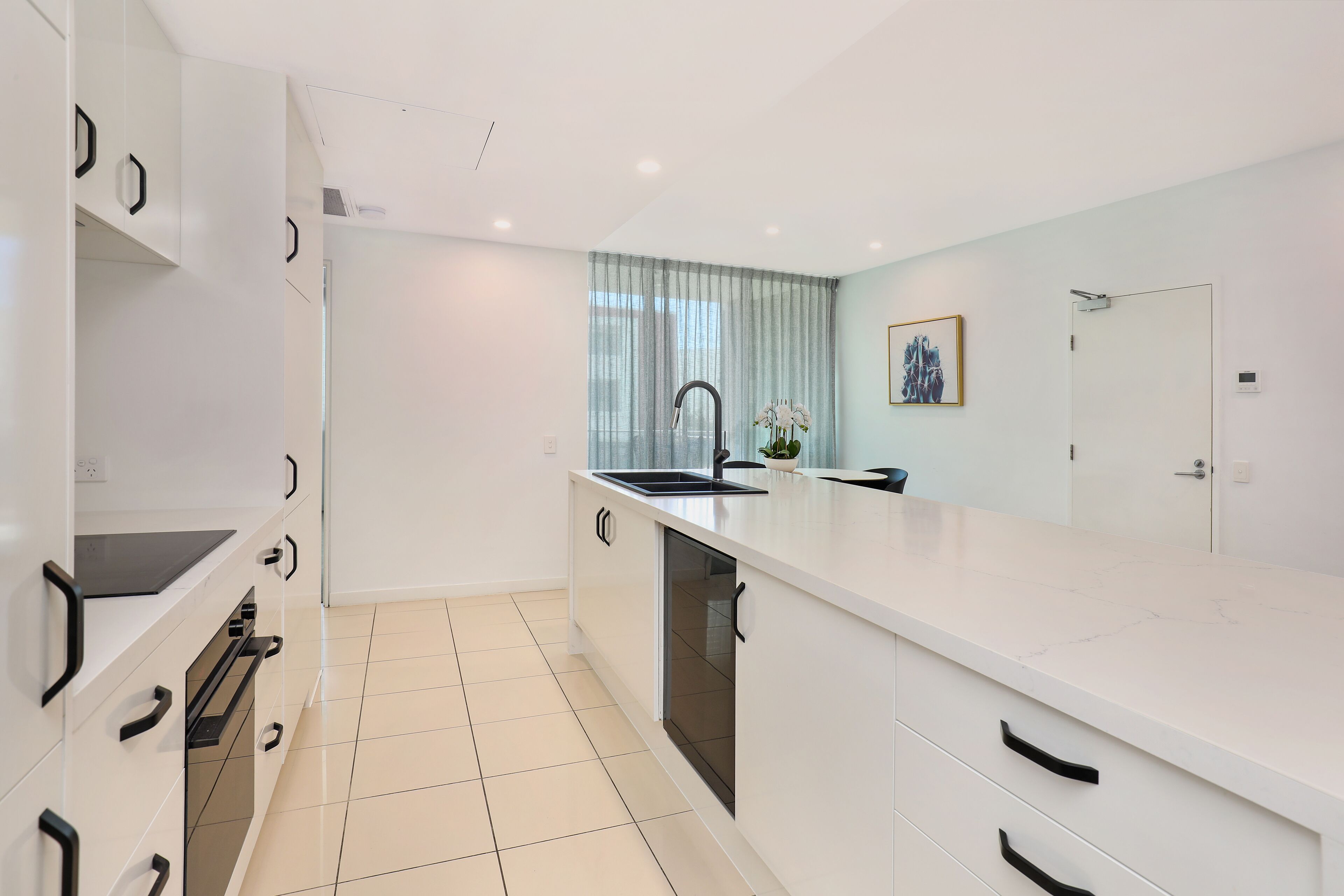 A modern kitchen with white cabinetry, a black faucet, and a large window with sheer curtains.