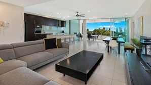 Un salon moderne avec un canapé d’angle, une table basse noire et un coin repas comprenant une table et des chaises.