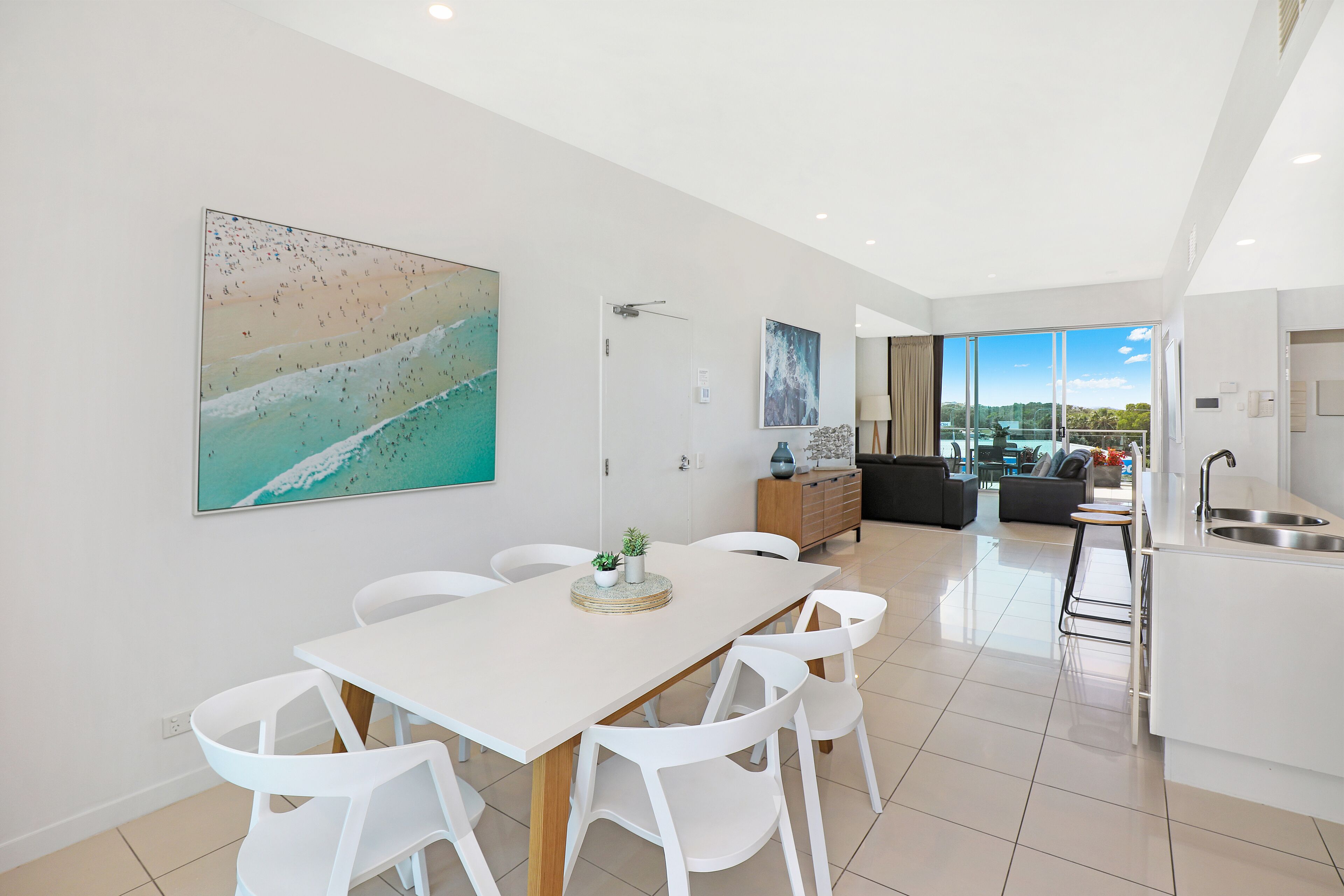 Una cocina moderna con una isla grande, un comedor con sillas blancas y un amplio ventanal con vistas al exterior.