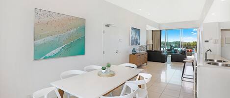 Una cocina moderna con una isla grande, un comedor con sillas blancas y un amplio ventanal con vistas al exterior.