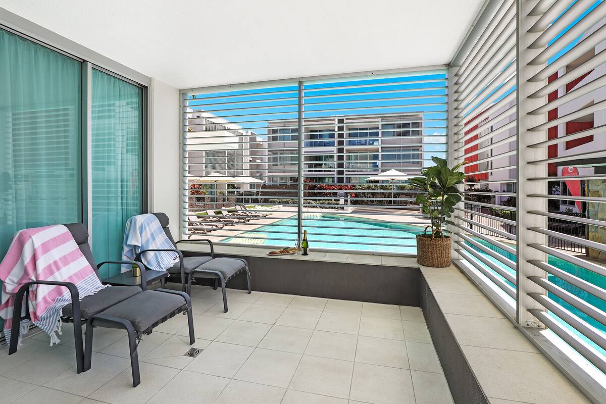 A balcony with a view of a swimming pool, lounge chairs, and a potted plant.