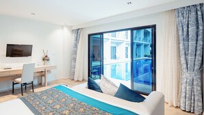 Habitación de hotel moderna con una cama grande, un escritorio, un televisor y un balcón con vista a la piscina.