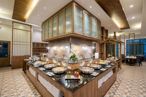 Zona de bufé con varias estaciones de comida, armarios de madera y piso de baldosas.