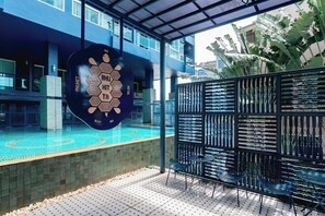 Un área de piscina con suelo de baldosas azules, un gran cartel circular con texto y una valla metálica con sillas.
