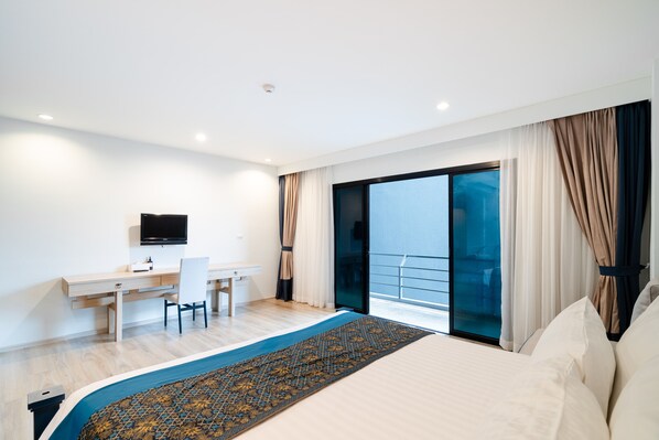 Una habitación de hotel moderna con una cama grande, un escritorio con silla, un televisor de pantalla plana y un balcón con cortinas.