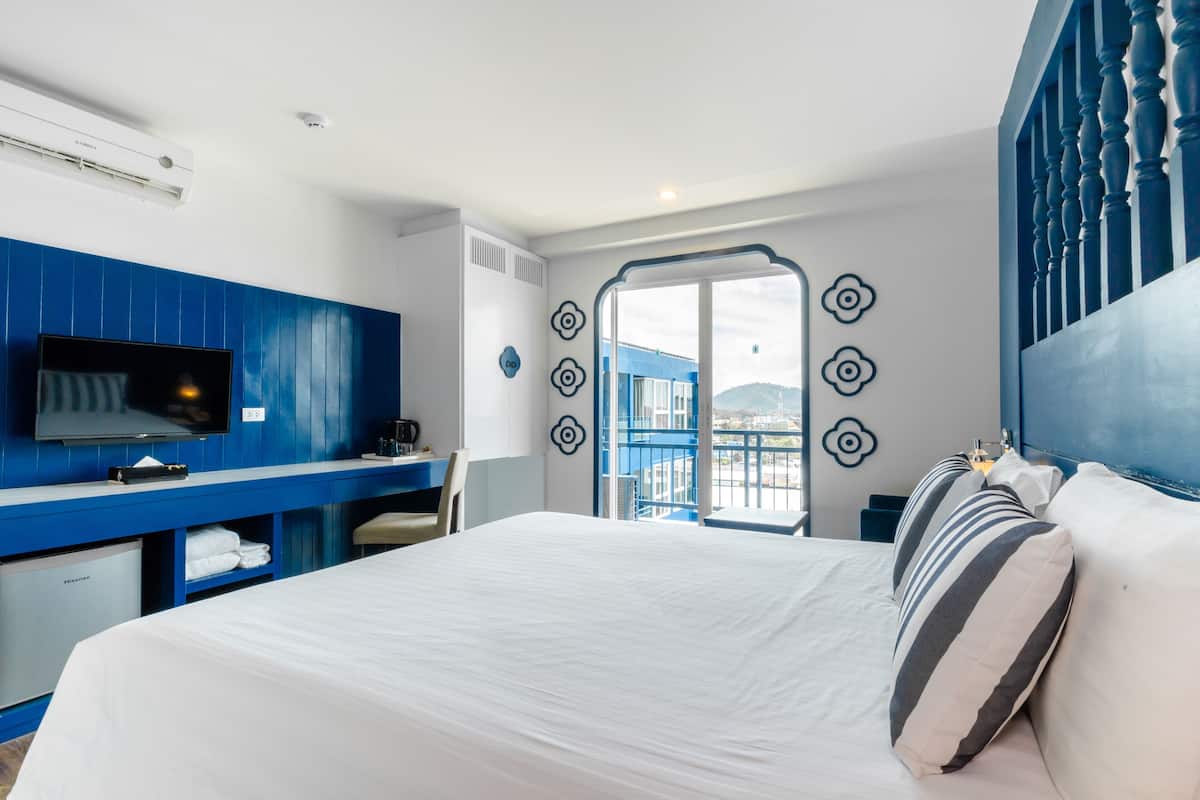Ett hotellrum med en säng, ett skrivbord, en tv och utsikt över staden.