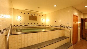 Een hotelbadkamer met een bad, betegelde muren en een houten deur.
