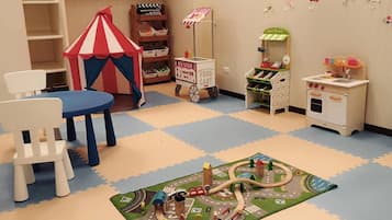 Children can play and learn in this vibrant playroom featuring a play kitchen, toy food cart, playhouse, and train set.