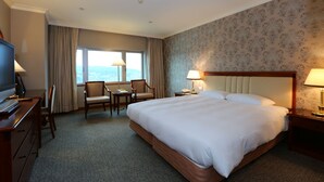 Een hotelkamer met een groot bed, een bureau met stoel, een televisie en een raam met gordijnen.