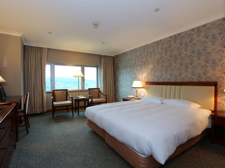A hotel room with a large bed, a desk with a chair, a television, and a window with curtains.
