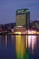 A high-rise hotel with multiple floors, illuminated windows, and a reflection in the water.