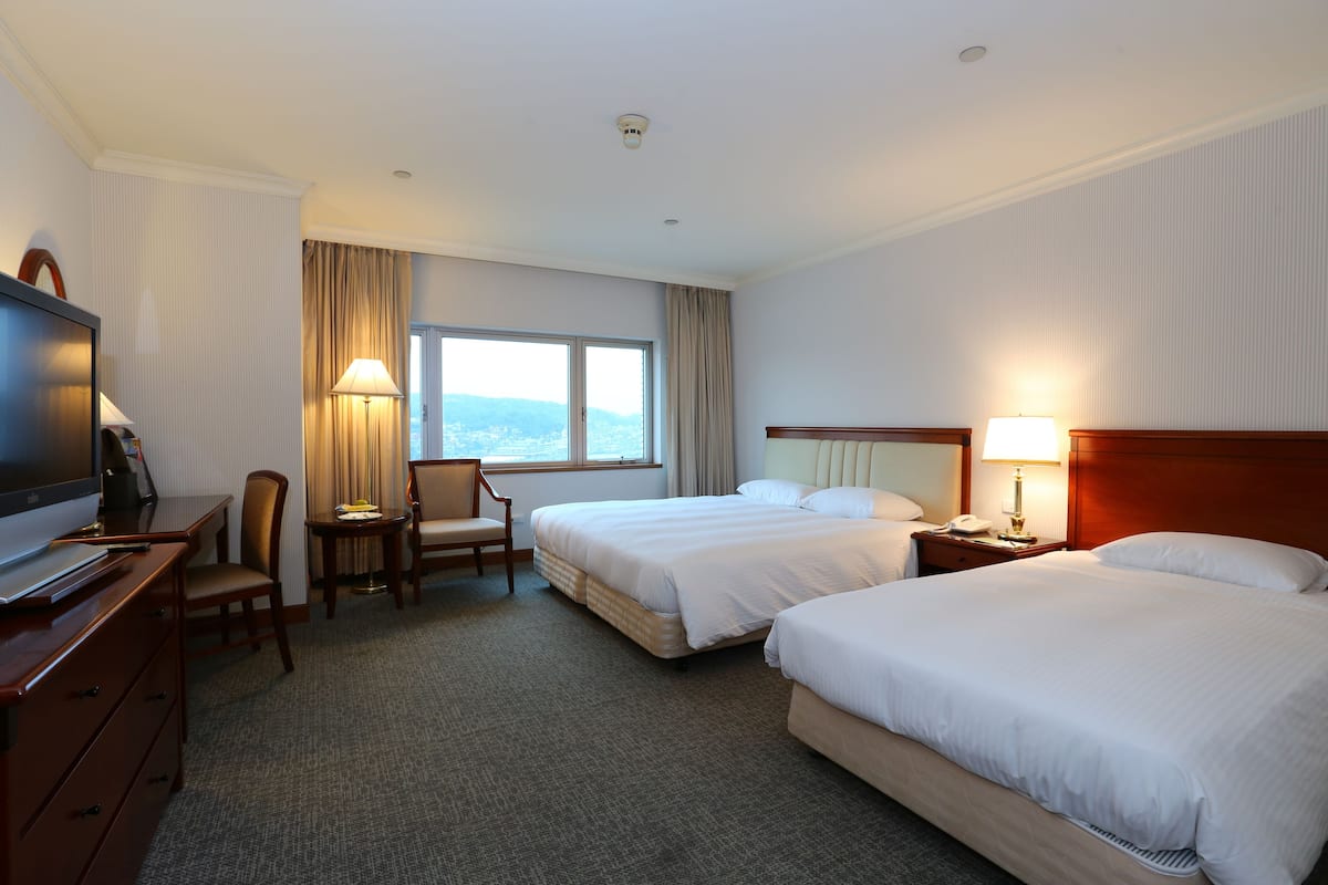 Een hotelkamer met twee bedden, een bureau met een televisie, een stoel, een lamp en een raam met gordijnen.