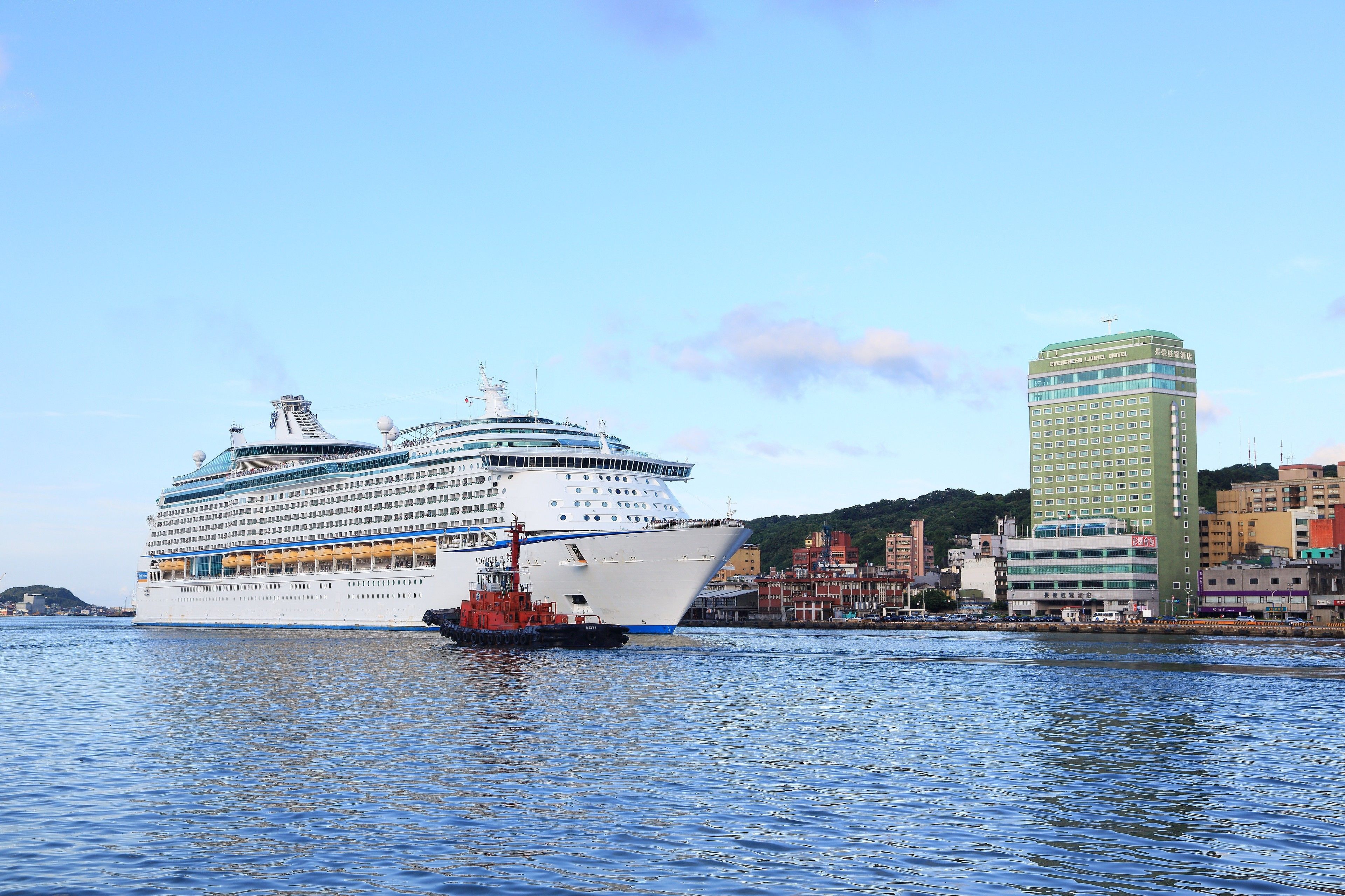 A large cruise ship docked at a port with a cityscape in the background.