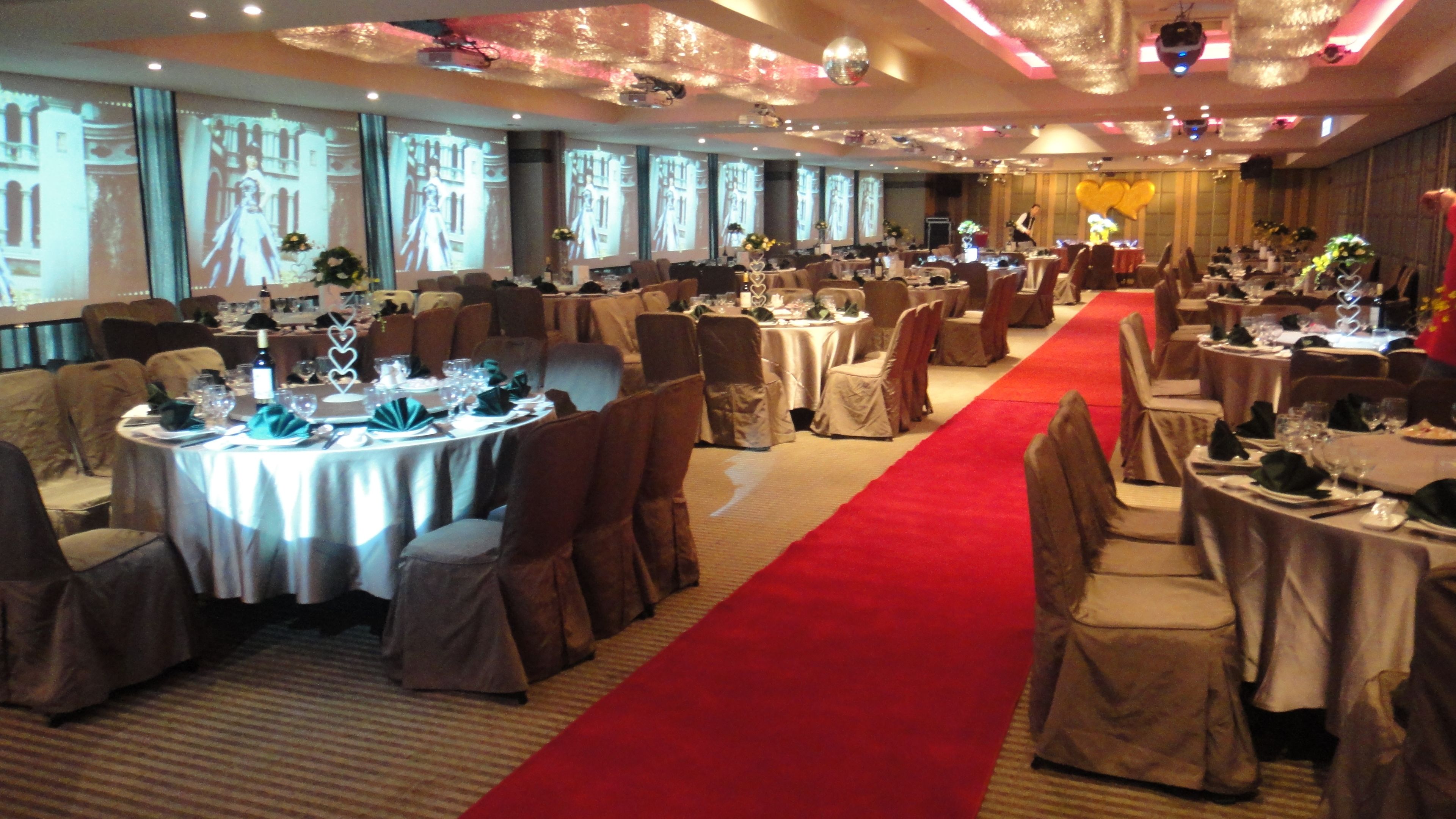 A banquet hall with round tables, red carpet, and projection screens on the walls.