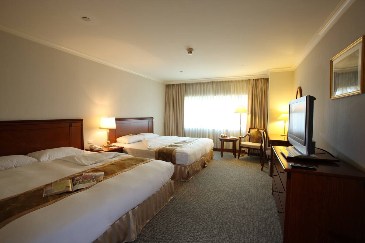 Een hotelkamer met twee bedden, een bureau met televisie, een stoel en een klein tafeltje met lamp.