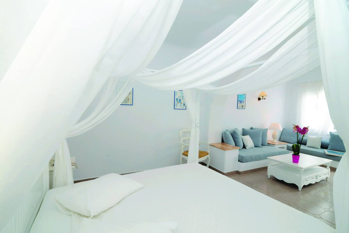 A bedroom with a bed, a white sofa, a coffee table, and a nightstand.