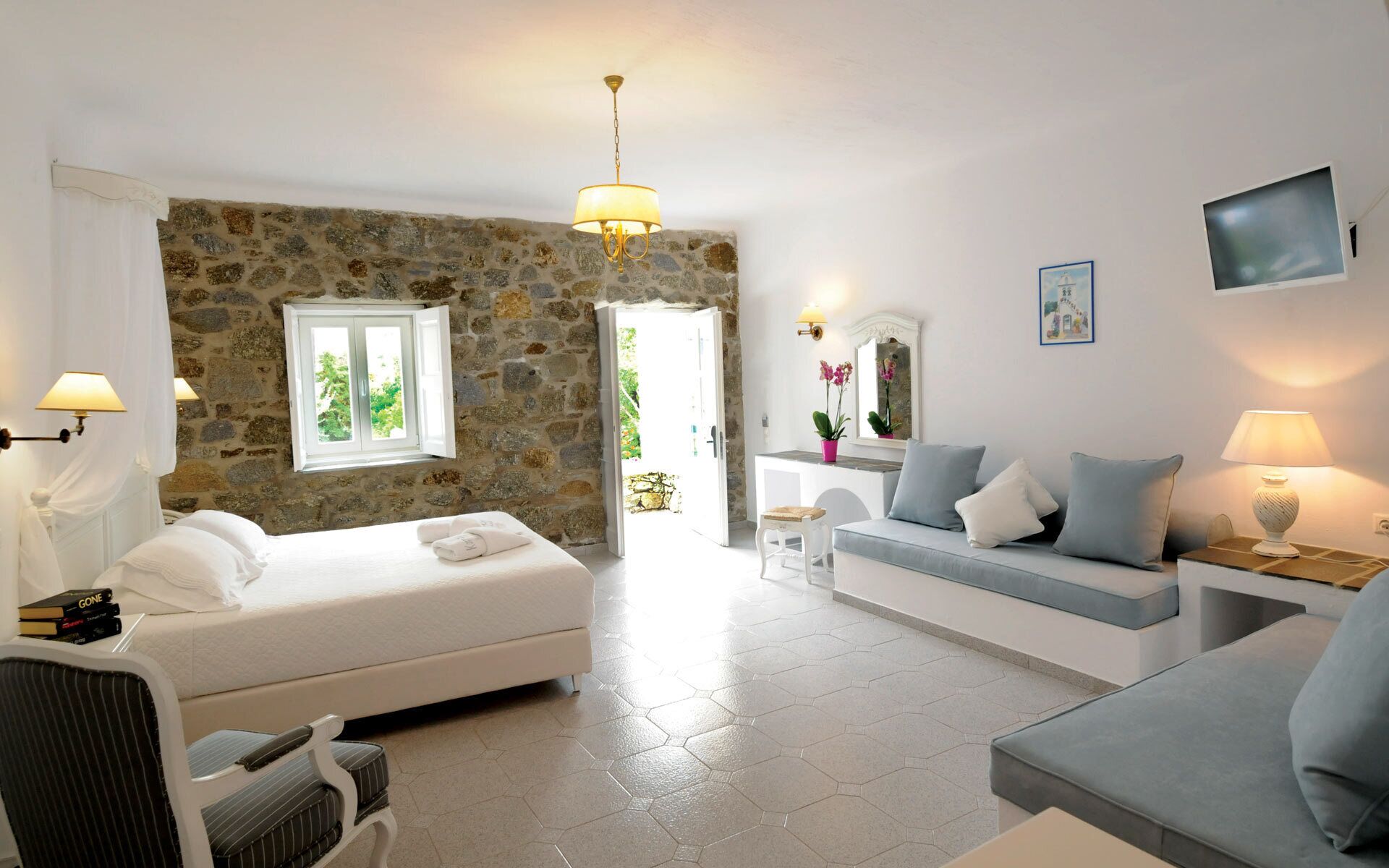A room with a stone wall, a bed, a sofa, a TV, and a window with curtains.