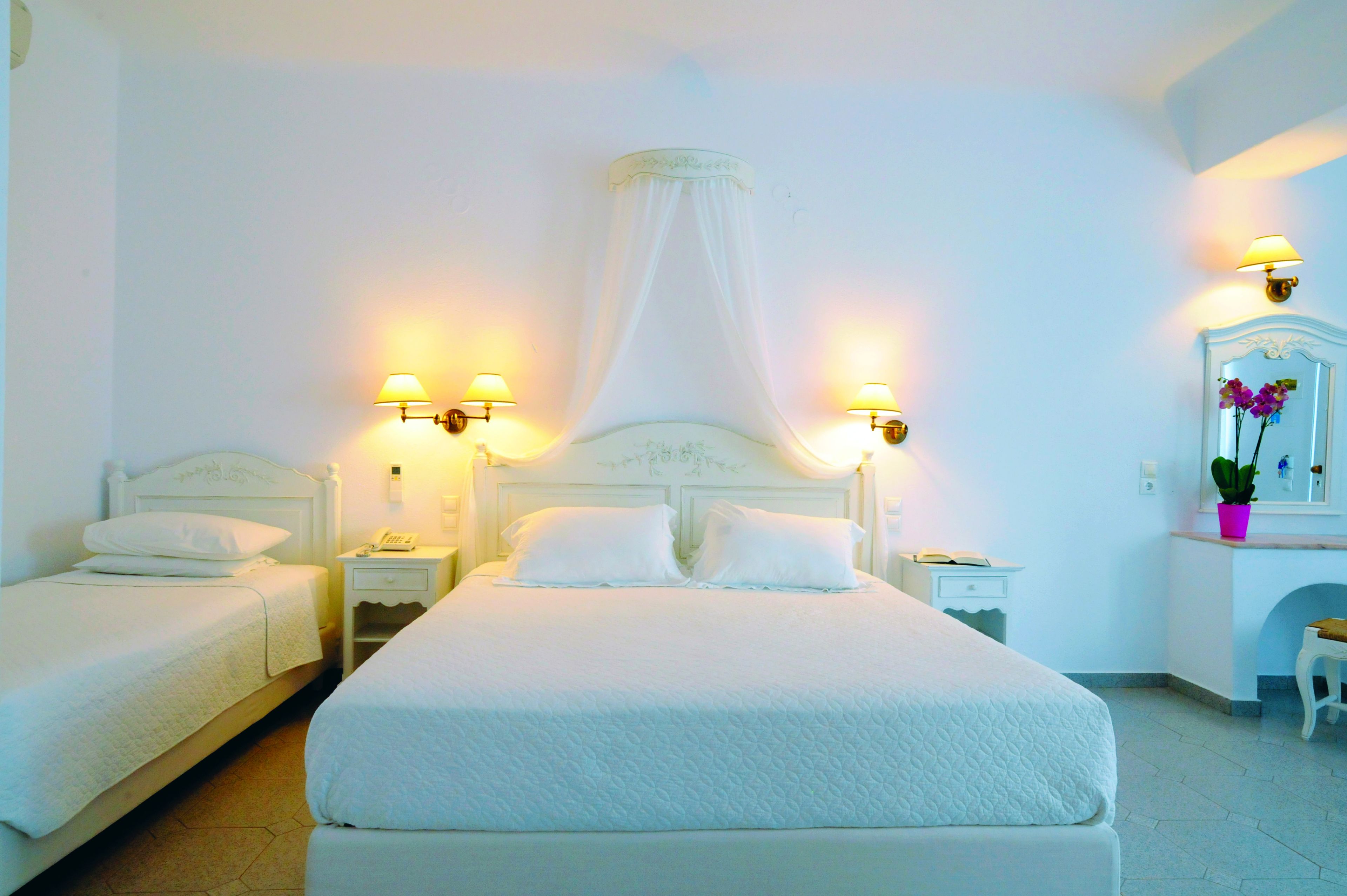 Una habitación de hotel con una cama grande, dos mesitas de noche, un taburete pequeño y un espejo.