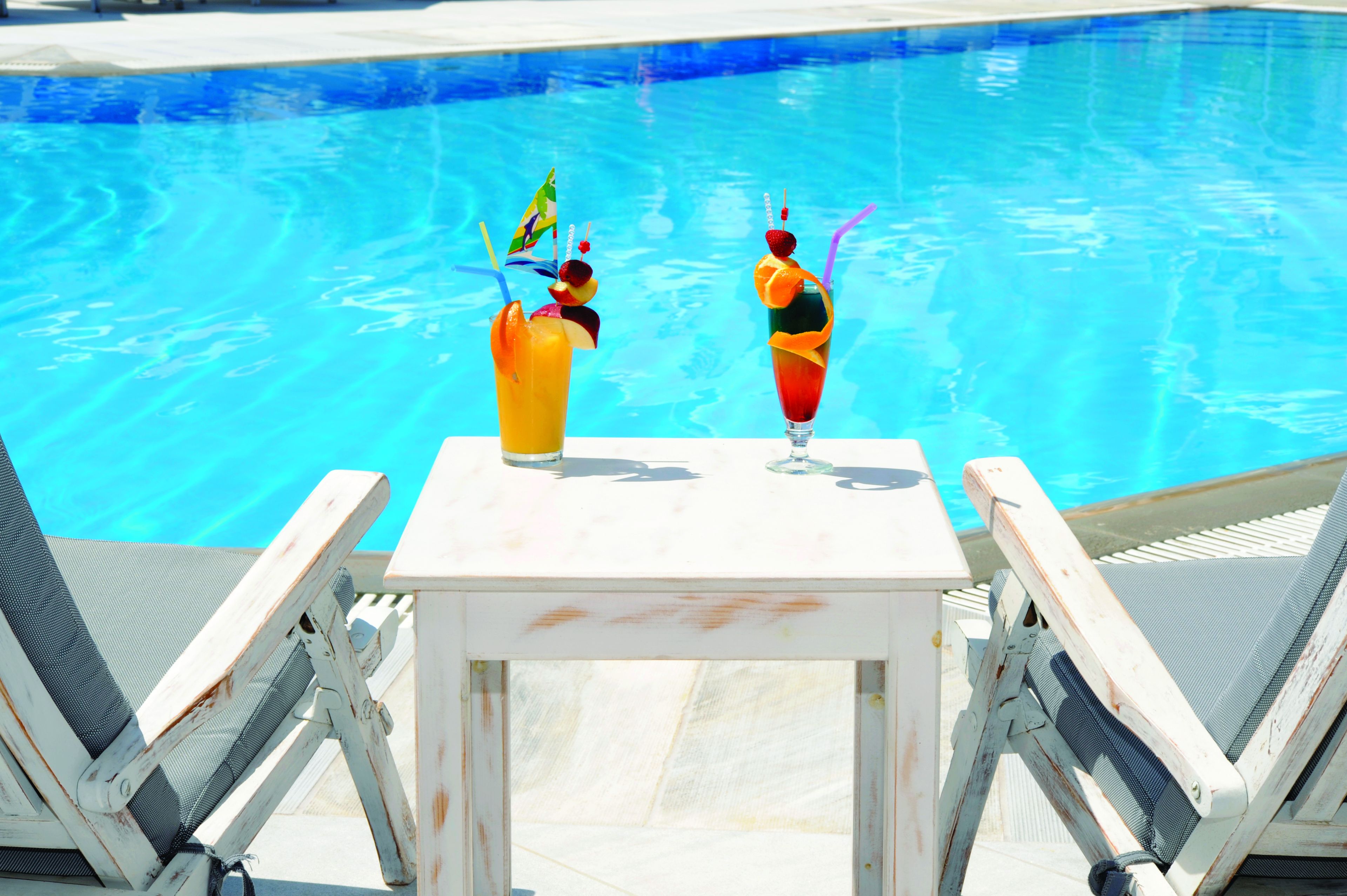 Une table placée au bord de la piscine, avec deux boissons et deux chaises longues.