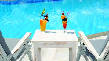 Une table placée au bord de la piscine, avec deux boissons et deux chaises longues.