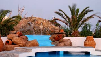 A pool area with a stone waterfall feature, surrounded by rocks and palm trees.
