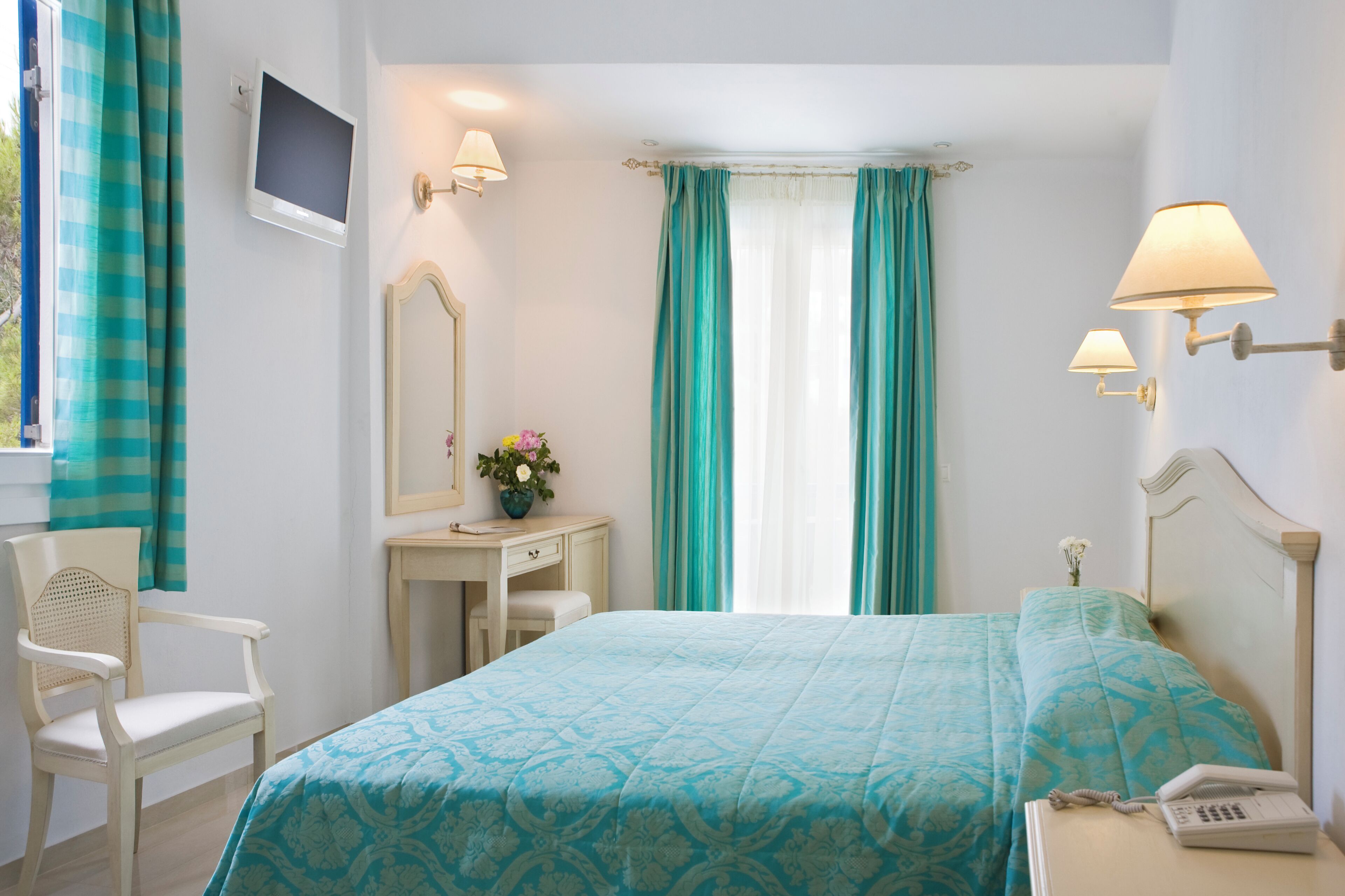 A hotel room with a bed, a desk, a chair, a TV, and a lamp.