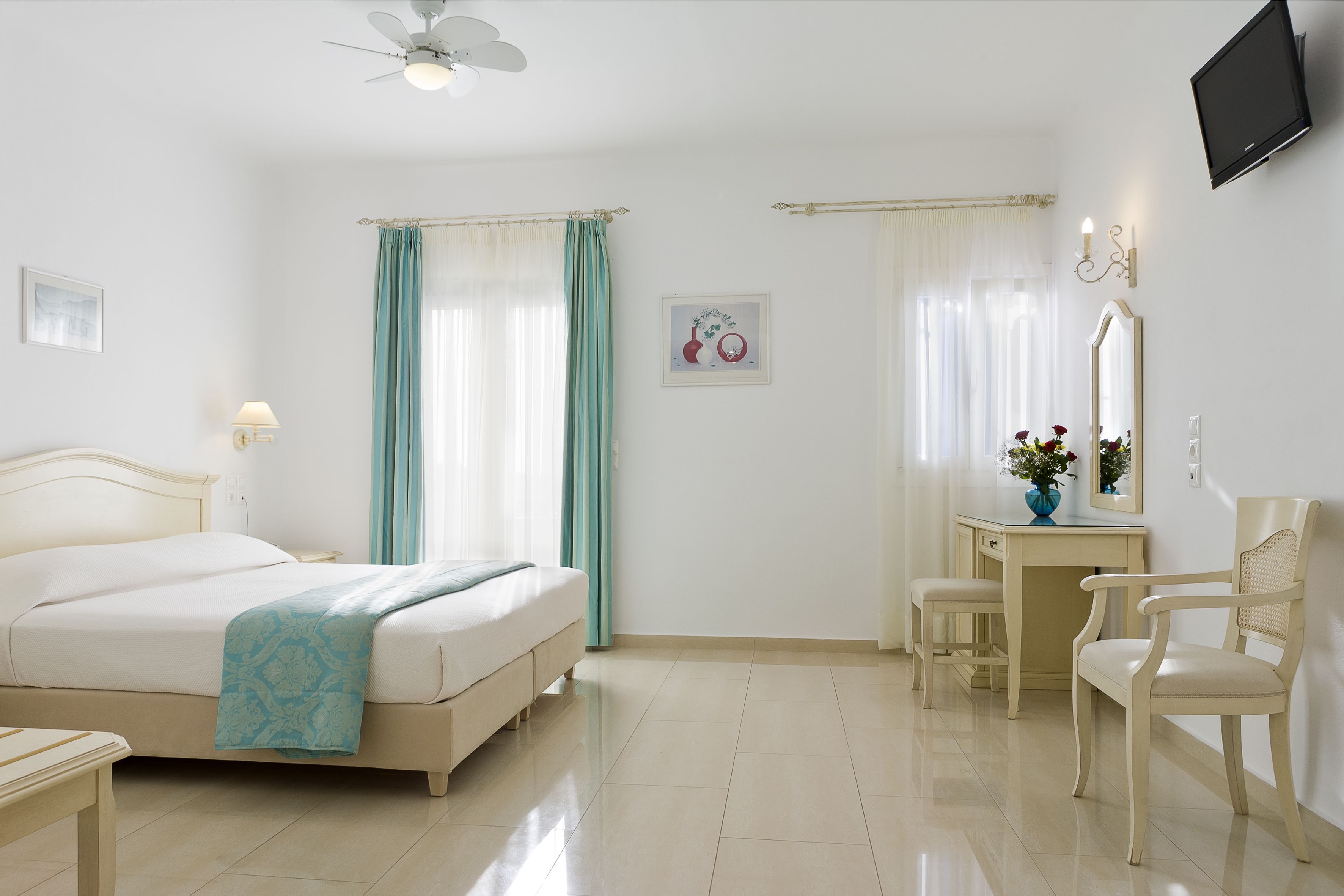 A hotel room with a bed, a desk, a chair, a TV, and a ceiling fan.
