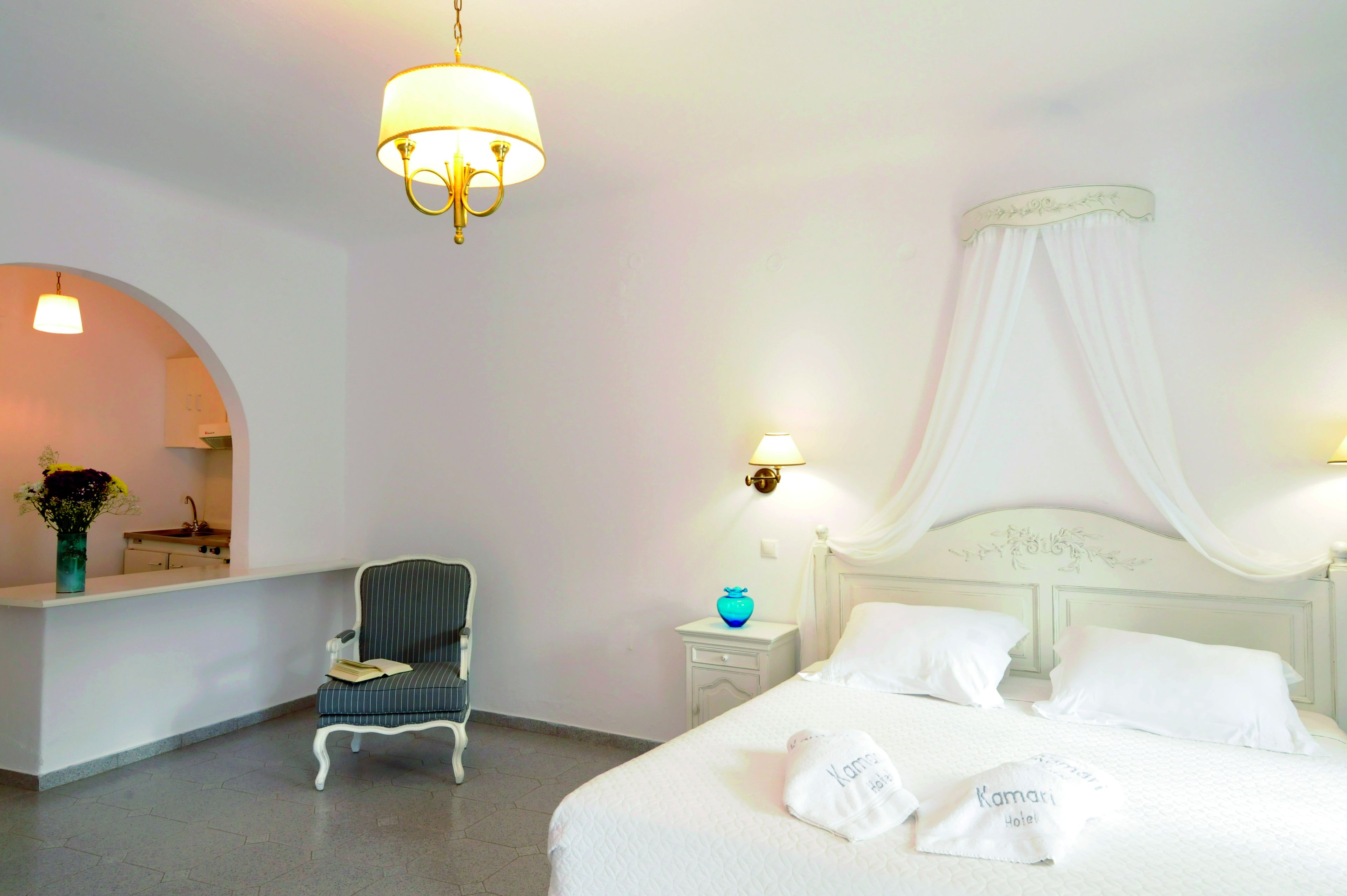 Una camera d'albergo con un letto, una sedia, un comodino, una lampada e uno specchio.