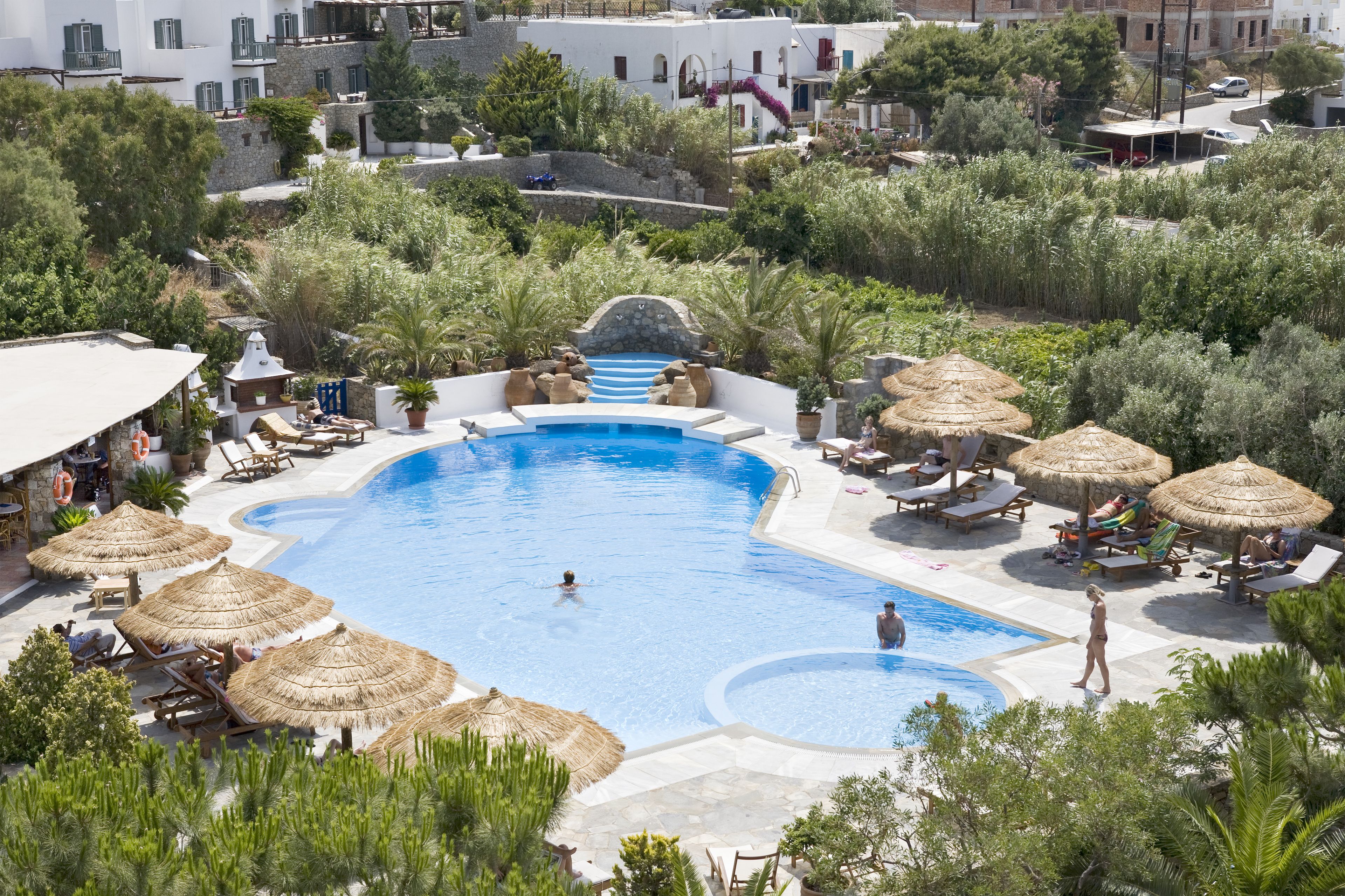 Una piscina con tumbonas y sombrillas, rodeada de vegetación y edificios.